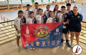 Jugadores infantiles y adultos en una pista cubierta, sosteniendo una bandera del Atlántico con logotipos de instituciones deportivas y del gobierno de Canarias, para un evento deportivo en Lanzarote.