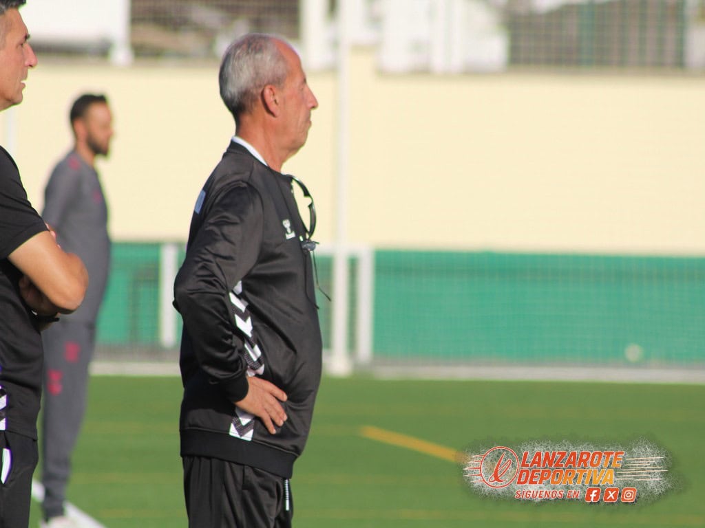 Entrenador y jugadores en un partido de fútbol en un campo de césped natural en Lanzarote.