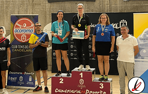 1. Jugadores en el podio de un torneo de tenis de mesa en Lanzarote, con medallas y trofeos, fondos con logos de patrocinadores y público en el gimnasio.