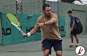 Jugador de tenis en acción en una cancha con malla, sosteniendo una raqueta y preparándose para golpear la pelota durante un partido en Lanzarote Deportivo.