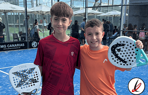 Jugadores niños con palas de pádel en una pista cubierta con público en el fondo, en Lanzarote Deportiva.