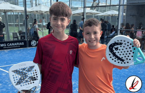 Jugadores niños con palas de pádel en una pista cubierta con público en el fondo, en Lanzarote Deportiva.