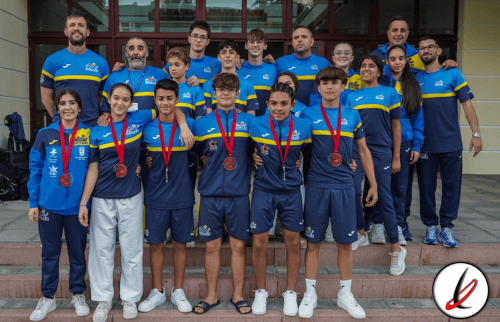 Campeones infantiles de baloncesto con medallas y entrenador en fondo de edificio, vestuarios azules y camisetas deportivas, celebrando victoria en torneo escolar en Lanzarote.