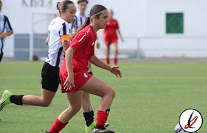 Coristas femeninas en un partido de rugby en Lanzarote, con jugadoras en movimiento en el campo, vestidas con uniformes deportivos y haciendo esfuerzos durante el juego en un día soleado.