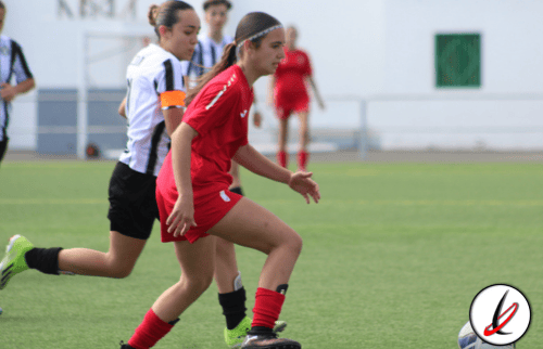 Coristas femeninas en un partido de rugby en Lanzarote, con jugadoras en movimiento en el campo, vestidas con uniformes deportivos y haciendo esfuerzos durante el juego en un día soleado.