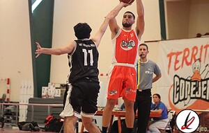 Bloqueo de jugador de baloncesto en partido en Lanzarote deportiva, jugador en acción con uniforme rojo saltando para bloquear a oponente, estadio y espectadores en fondo.