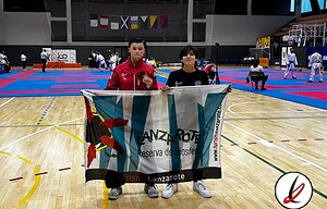 1. Dos jóvenes deportistas en un pabellón cubierto de Lanzarote con bandera y medallas tras una competición de artes marciales.