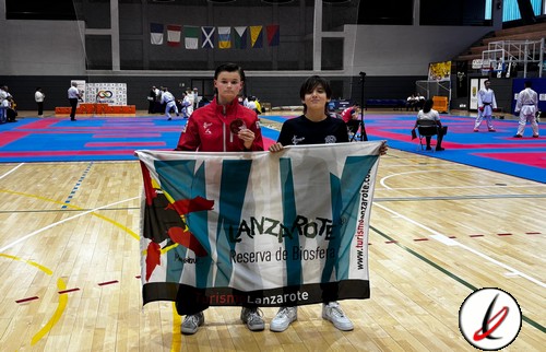 1. Dos jóvenes deportistas en un pabellón cubierto de Lanzarote con bandera y medallas tras una competición de artes marciales.