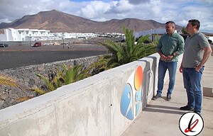 Jugadores conversando junto a un mural en Lanzarote con fondo de volcanes y ciudad, en un entorno al aire libre con cielo despejado y clima soleado, en un día caluroso.