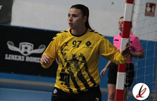 1. Jugadora de balonmano en acción, con camiseta amarilla número 97, en juego en un partido en interiores, con fondo de pista y árbitros.