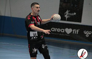 Un jugador de fútbol sala en acción, preparado para pasar el balón en una pista cubierta de deporte, con uniforme negro y detalles rojos, dentro de un estadio deportivo.