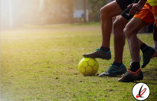 1. Dos niños jugando al fútbol en un campo de césped, concentrados en el balón, con luz natural y fondo difuso de entorno deportivo.