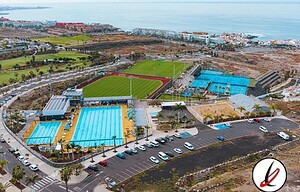 Bañera de piscina al aire libre en Lanzarote, con espectadores y zonas de descanso, vista aérea de instalaciones deportivas en un entorno costero con playa y mar al fondo.