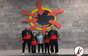 Un grupo de cinco personas, incluyendo niños y adultos, posando frente a un mural de Lanzarote con forma de sol y figuras humanas en la isla.