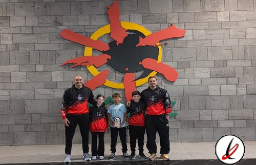 Un grupo de cinco personas, incluyendo niños y adultos, posando frente a un mural de Lanzarote con forma de sol y figuras humanas en la isla.
