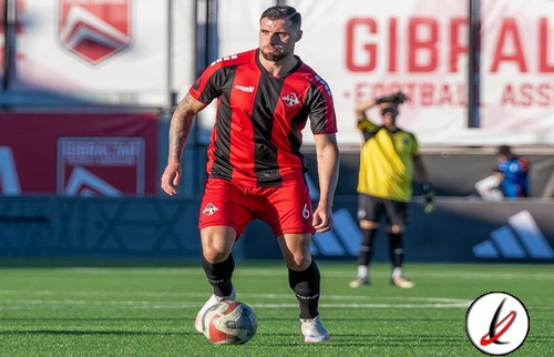 1. Jugador de fútbol con camiseta roja y negra controlando el balón en el campo durante un partido.