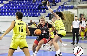 1. Jugadora de baloncesto en acción en una cancha cubierta, rodeada de otras jugadoras, algunos árbitros y espectadores en los asientos azules del estadio.