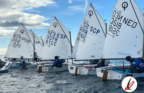 1. Velas de vela ligera en el agua con deportistas navegando bajo un cielo nublado, en un día brillante, en Lanzarote, durante una competición de vela en el mar.
