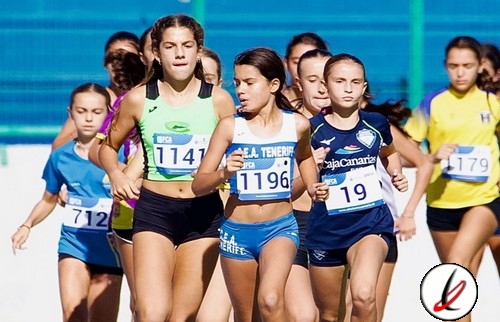Corredoras en una competición atlética en un estadio, portando ropa deportiva y números de carrera, destacando la concentración y esfuerzo en la pista de Lanzarote Deportiva.