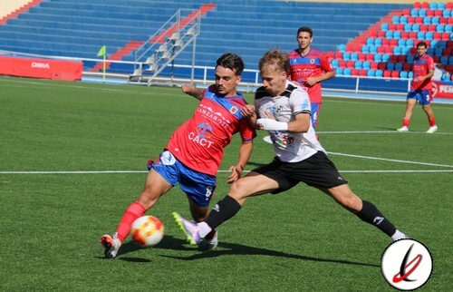 Lucha por el balón entre dos futbolistas en un partido en un estadio de Lanzarote, con público en las gradas y césped bien cuidado. Jugadores en acción durante un partido de fútbol en un campo profesional.