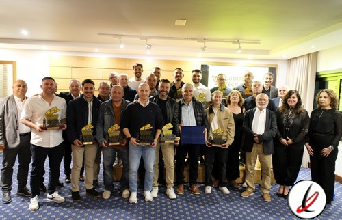 1. Grupo de personas en un evento, algunas sosteniendo trofeos, en una sala con fondo de pantalla y logotipo de Lanzarote Deportiva, en celebración o reconocimiento.