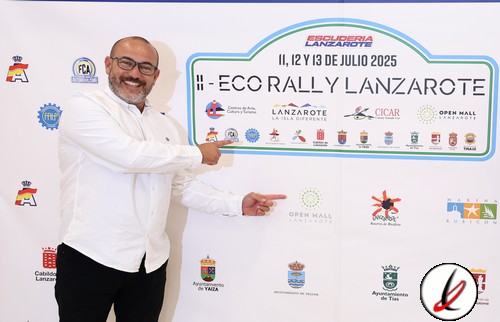 1. Persona en una reunión oficial sosteniendo un cartel del Eco Rally Lanzarote 2025, con logotipos y patrocinadores en el fondo, vestido con camisa blanca y gafas, en un ambiente formal y festivo.