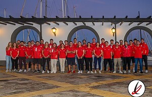 Jugadores del equipo de Lanzarote Deportiva posando en un puerto con fondo de veleros y arquitectura marina, todos con camiseta roja, en una foto grupal al atardecer.