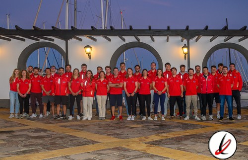 Jugadores del equipo de Lanzarote Deportiva posando en un puerto con fondo de veleros y arquitectura marina, todos con camiseta roja, en una foto grupal al atardecer.