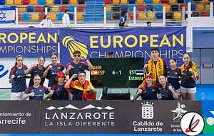Jugadoras de balonmano del equipo nacional español en la pista durante un partido de campeonato europeo, con pancarta y logo del campeonato visible en el fondo.
