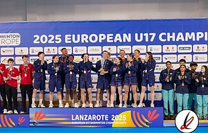La imagen muestra a un grupo de jugadores de bádminton juvenil celebrando en el podio del Campeonato Europeo Sub-17 2025 en Lanzarote, con uniforme azul y varios jugadores sosteniendo medallas, en un escenario con cartel de fondo y logotipos de patrocinadores.