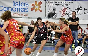 1. Jugadoras de baloncesto en acción durante un partido en una cancha cubierta, con el público y banners publicitarios visibles en el fondo.