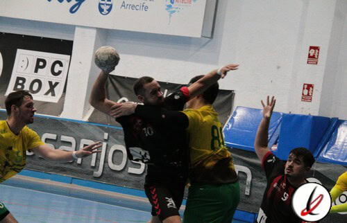 1. Jugador de balonmano lanzando el balón en un partido en el pabellón de Lanzarote, con rivales y espectadores en el fondo.