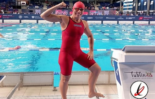 Una nadadora con traje rojo, gorro y gafas levantando el brazo en una piscina de competición.