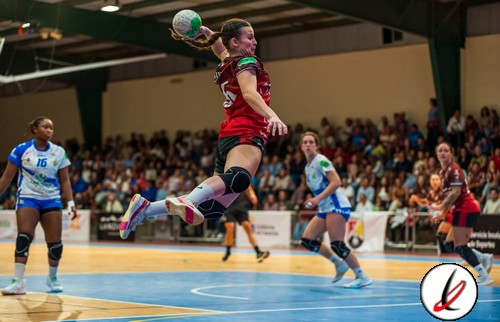 1. Jugadora de balonmano en acción en interior, saltando para lanzar el balón con fuerza durante un partido en cancha cubierta.