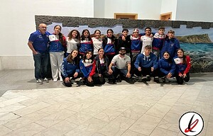Jugadores de un equipo de baloncesto con uniforme, en una presentación en un entorno interior con fondo decorativo de paisaje marítimo y entrenador a la izquierda.