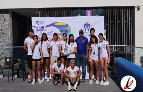 1. Equipo femenino de voleibol de Lanzarote posando junto a su entrenador en un evento deportivo.