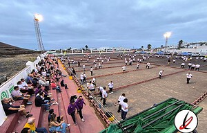 Jugadores y espectadores en un estadio de beach volley en Lanzarote, con actividades en curso y un ambiente animado bajo un cielo nublado.
