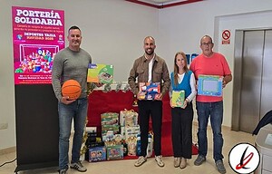 Jóvenes donando regalos en un acto solidario en LanzaroteDeportiva, con una mesa de regalos y un cartel de "Portería Solidaria" en un entorno interior con ascensor y paredes blancas.