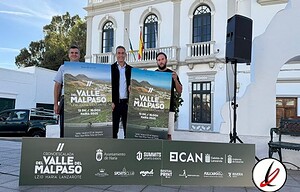 1. Tres hombres en un acto oficial sosteniendo carteles promocionales para una carrera en Lanzarote, en un entorno urbano con edificio histórico y escenario al aire libre.