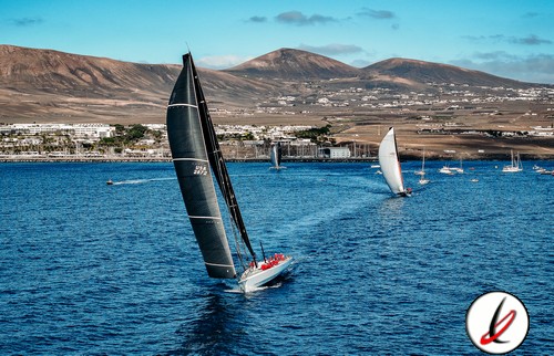 Vela en Lanzarote, deporte náutico en el mar con veleros grandes en agua azul, montañas al fondo y cielo despejado, en un día soleado y ventoso.