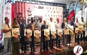 1. Grupo de personas en un escenario con fondos de eventos deportivos y banderas, sosteniendo carteles promocionales en un acto oficial.