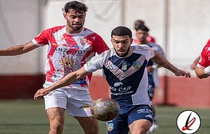 Un jugador del equipo con camiseta blanca y azul lucha por el balón con un rival con camiseta roja en un partido de fútbol en el campo de Lanzarote Deportiva.
