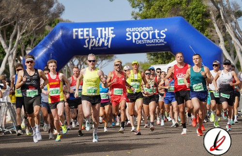 Corredores participando en una maratón en Lanzarote, con un arco de salida con las palabras "Feel the Spirit" y "European Sports Destination" en un día soleado.