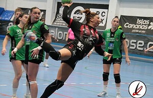 Una jugadora de balonmano en acción, saltando para lanzar el balón durante un partido femenino en un pabellón deportivo. Jugadoras en uniforme verde y negro en el fondo, en un partido de deportes en Lanzarote.