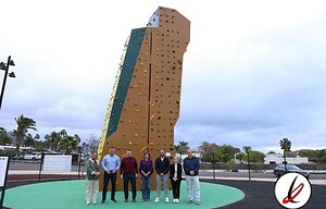 Escalador en parque de deporte al aire libre en Lanzarote, con estructura de rocódromo en fondo, personas posando y cielo nublado en día soleado.