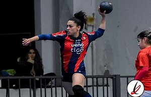 Arbusera feminina de balonmano en acción durante un partido en un pabellón cubierto, con jugadora en movimiento lanzando un balón, mostrando concentración y esfuerzo.