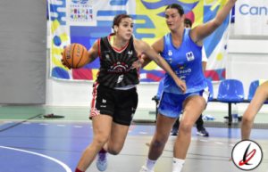 1. Jugadora de baloncesto en acción durante un partido en una cancha cubierta, con otra jugadora defensora y público de fondo.