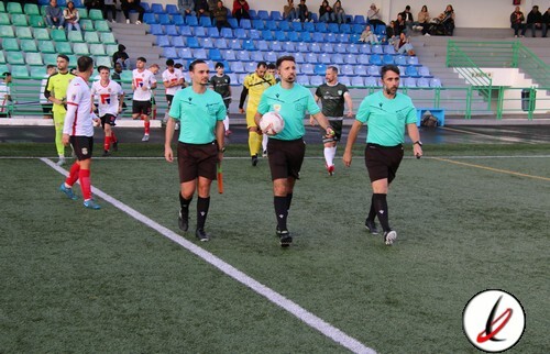 Árbitros caminando hacia el campo de fútbol antes del inicio del partido en Lanzarote Deportiva. Jugadores y espectadores en las gradas del estadio, preparado para un partido de fútbol.