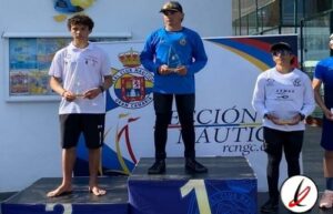 Niño en el podio de una competencia deportiva, recibiendo premio, con fondo de cartel y otros niños en la ceremonia.