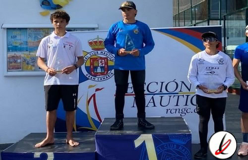 Niño en el podio de una competencia deportiva, recibiendo premio, con fondo de cartel y otros niños en la ceremonia.